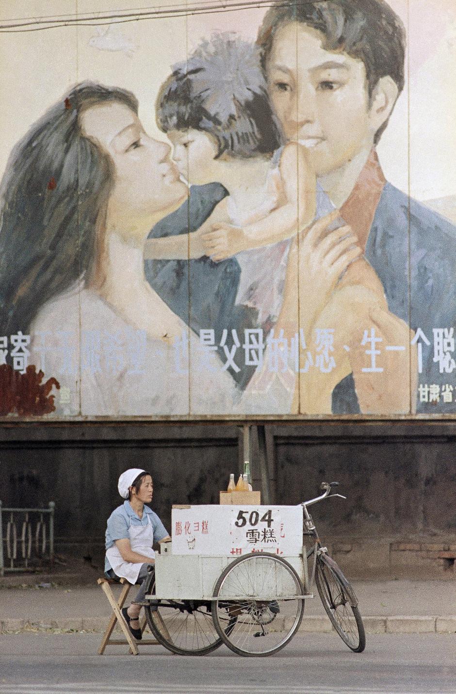 A street vendor awaits customers beneath a billboard exhorting people to adhere to China's one-child policy, in Lanzhou, China on August 4, 1988. China recently lifted the policy, allowing families to have a second child. Mark Avery/AP